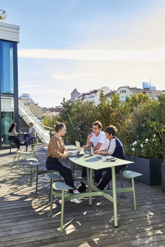 Bolder 3-Sitzer Tisch mit Sitzflächen von Fermob im Außenbereich mit drei Personen, ideal für Büroterrassen.