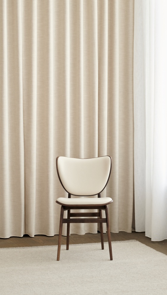 Vollgepolsterter Elephant Dining Chair Stuhl von NORR11 mit Holzrahmen und beigem Bezug vor Vorhang.