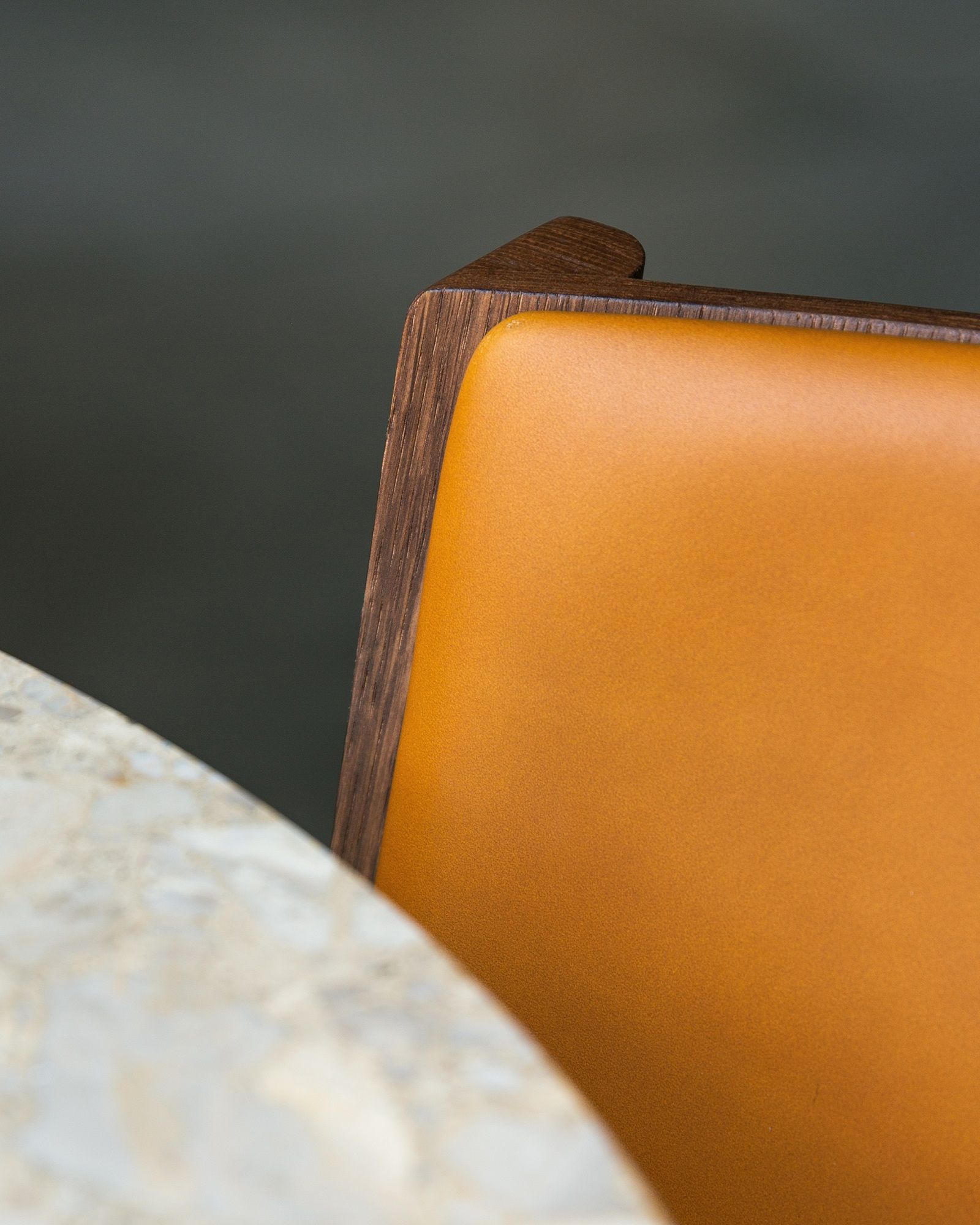 Detailaufnahme des Audo Copenhagen Ready Dining Chair mit braunem Holzrahmen und orangefarbener Polsterung neben einem Marmortisch.