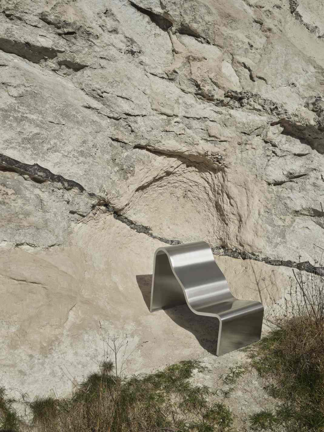 Muuto Dream Bench Outdoor Bank aus gebogenem Edelstahl vor einer Felswand.