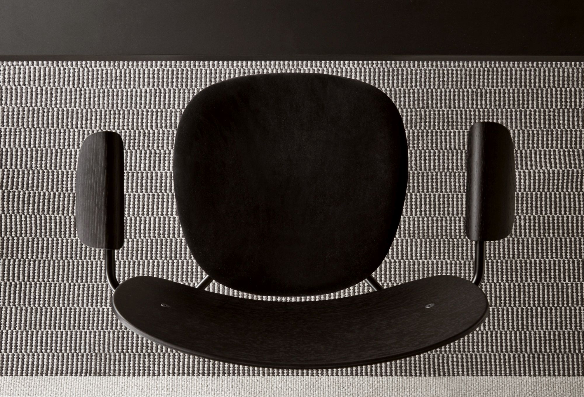Draufsicht des schwarzen Co Dining Chair Stuhls von Audo Copenhagen auf einem gemusterten Teppich.