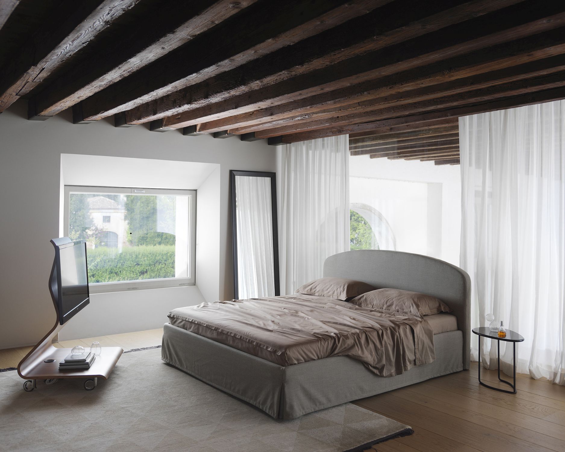 Schlafzimmer Interieur mit Yume Black Spiegel von Casamania Horm, Bett, Fenster und Holzbalkendecke.