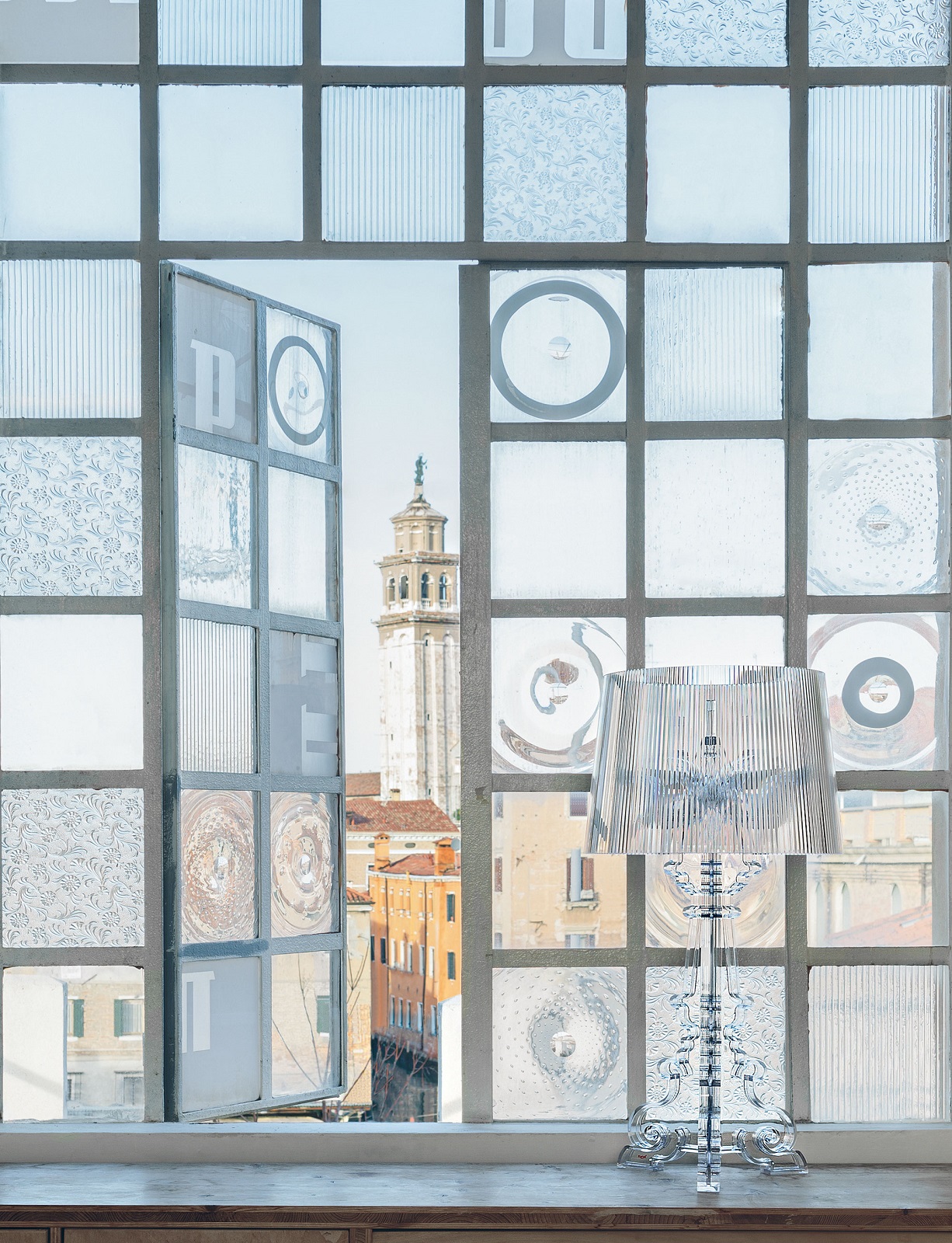 Nahaufnahme der Kartell Bourgie Tischleuchte in glasklar vor einem Fenster mit Blick auf Venedig.