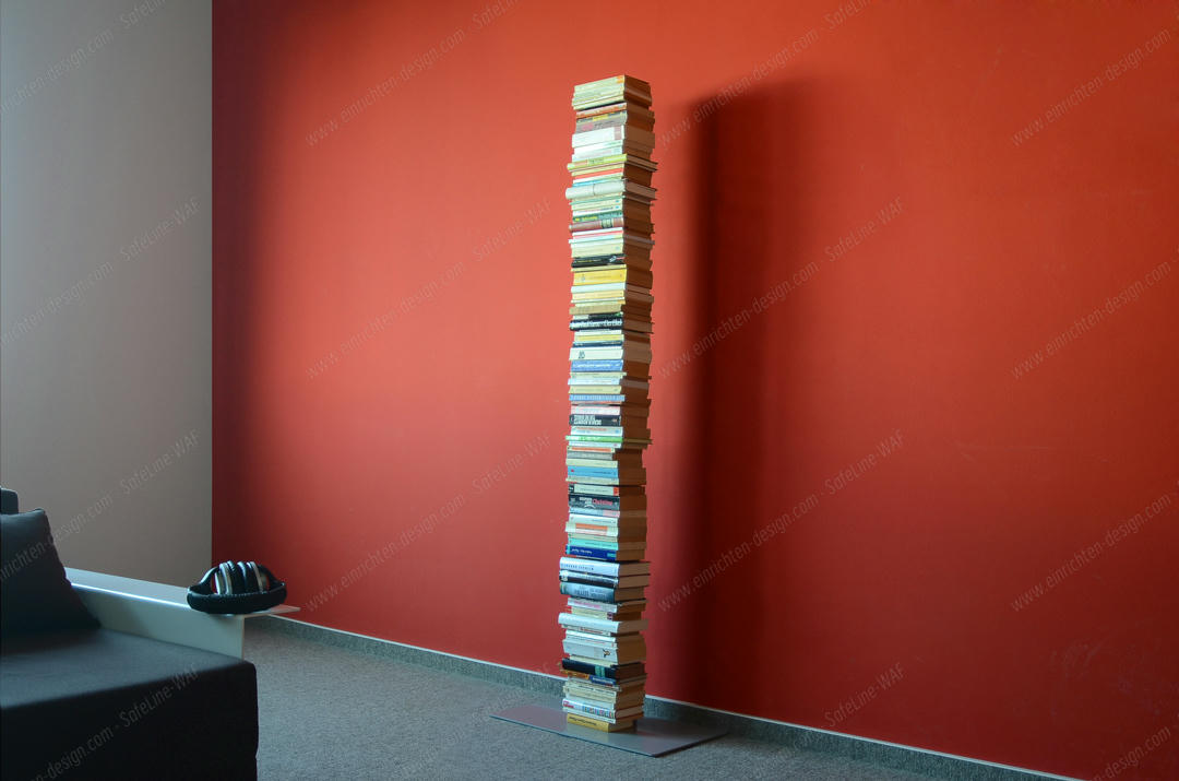 Booksbaum Standregal: Hoher Bücherstapel als Design-Regal vor roter Wand. Bücherregal, Möbel für Wohnzimmer.