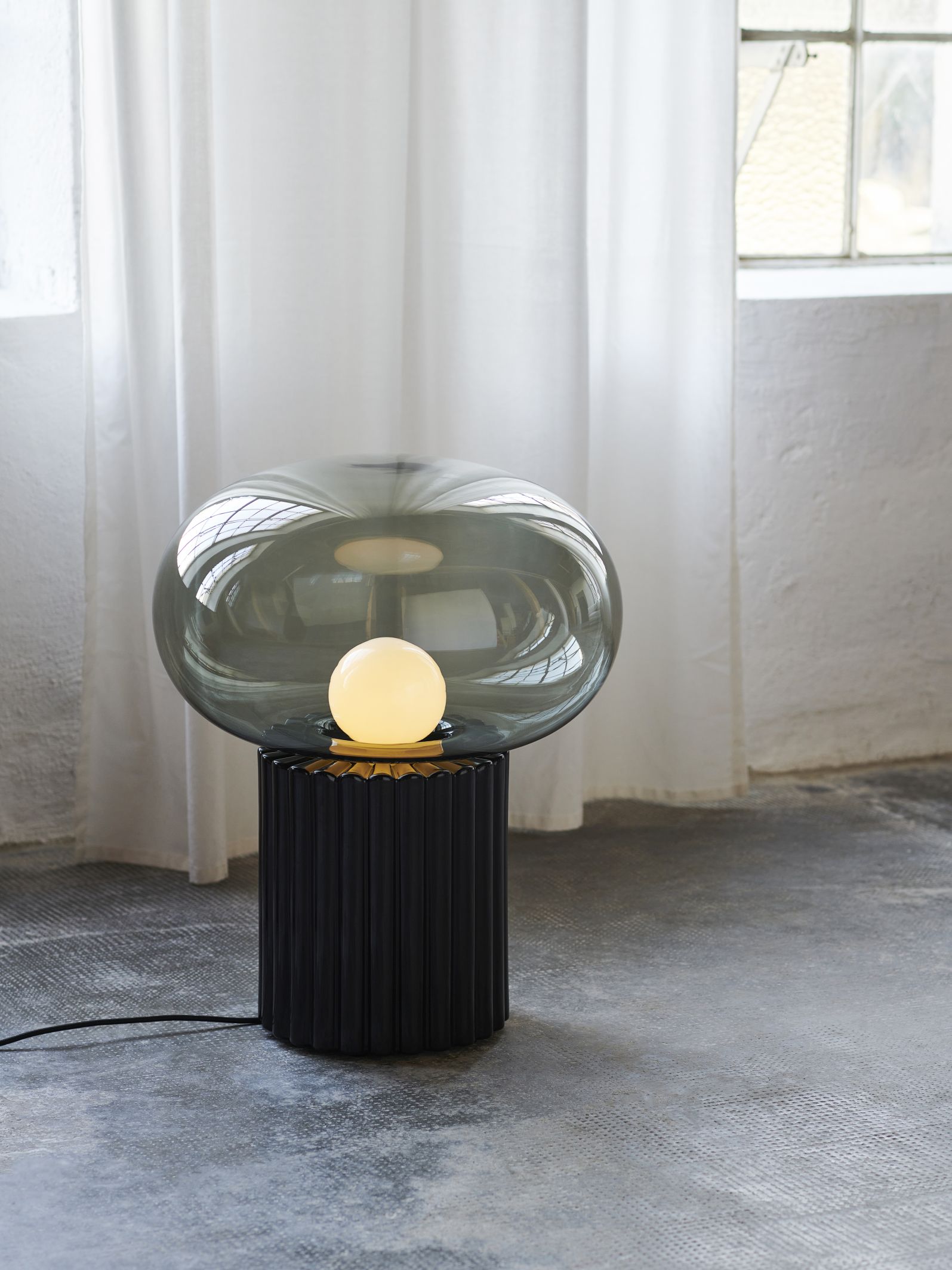 Fungi Bodenleuchte Favius Schwarz: Moderne Stehlampe mit rauchglasfarbenem Schirm und geriffeltem, schwarzem Sockel.