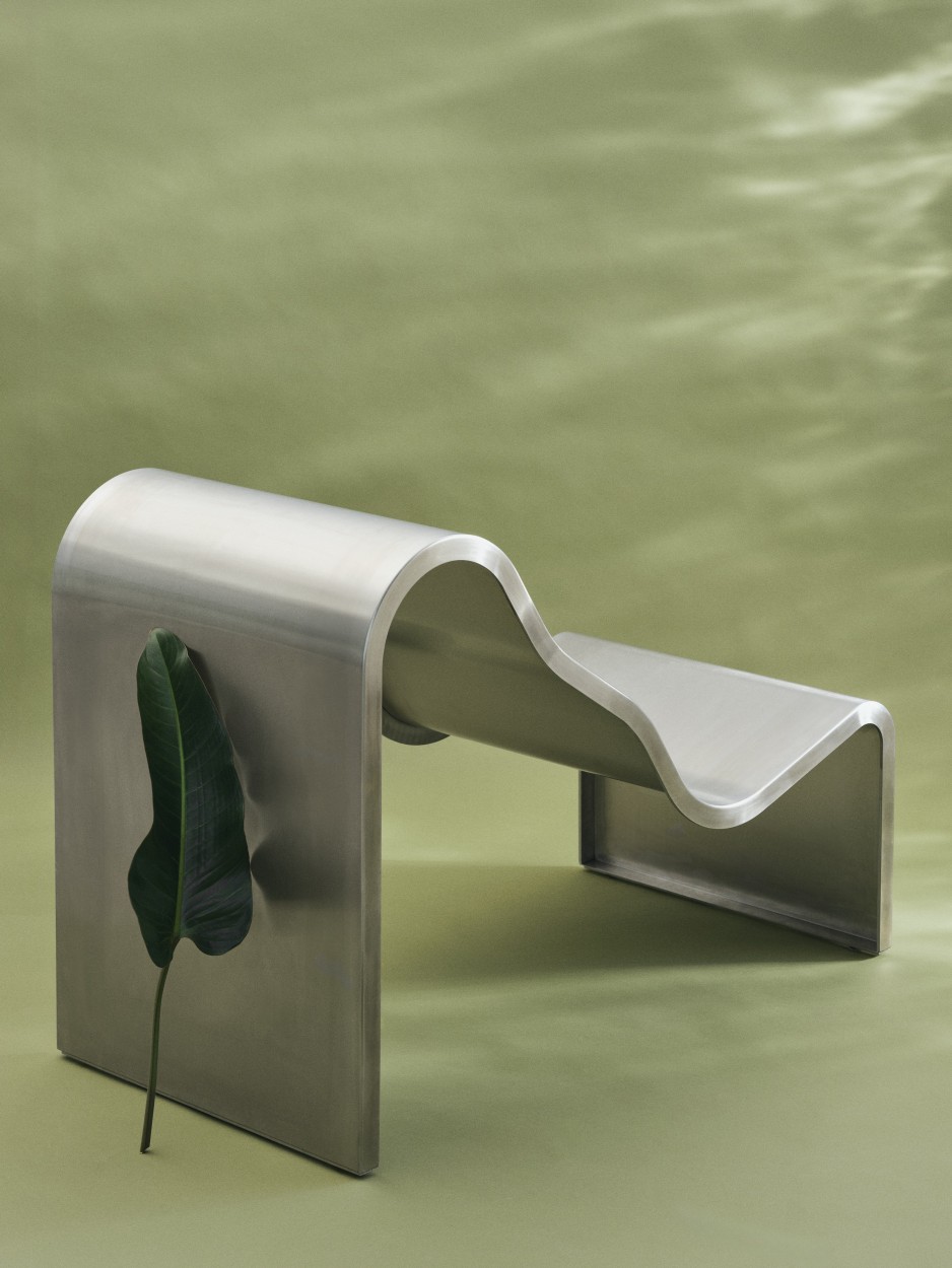 Muuto Dream Bench: Moderne Indoor/Outdoor Bank aus gebogenem Metall mit Blatt auf grünem Hintergrund.