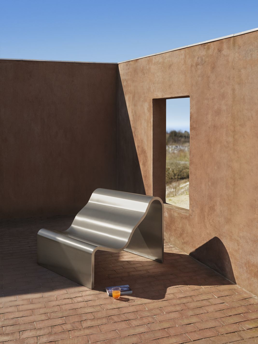 Muuto Dream Bench Indoor/Outdoor Bank aus poliertem Edelstahl auf Backsteinterrasse, mit Getränk und Buch.