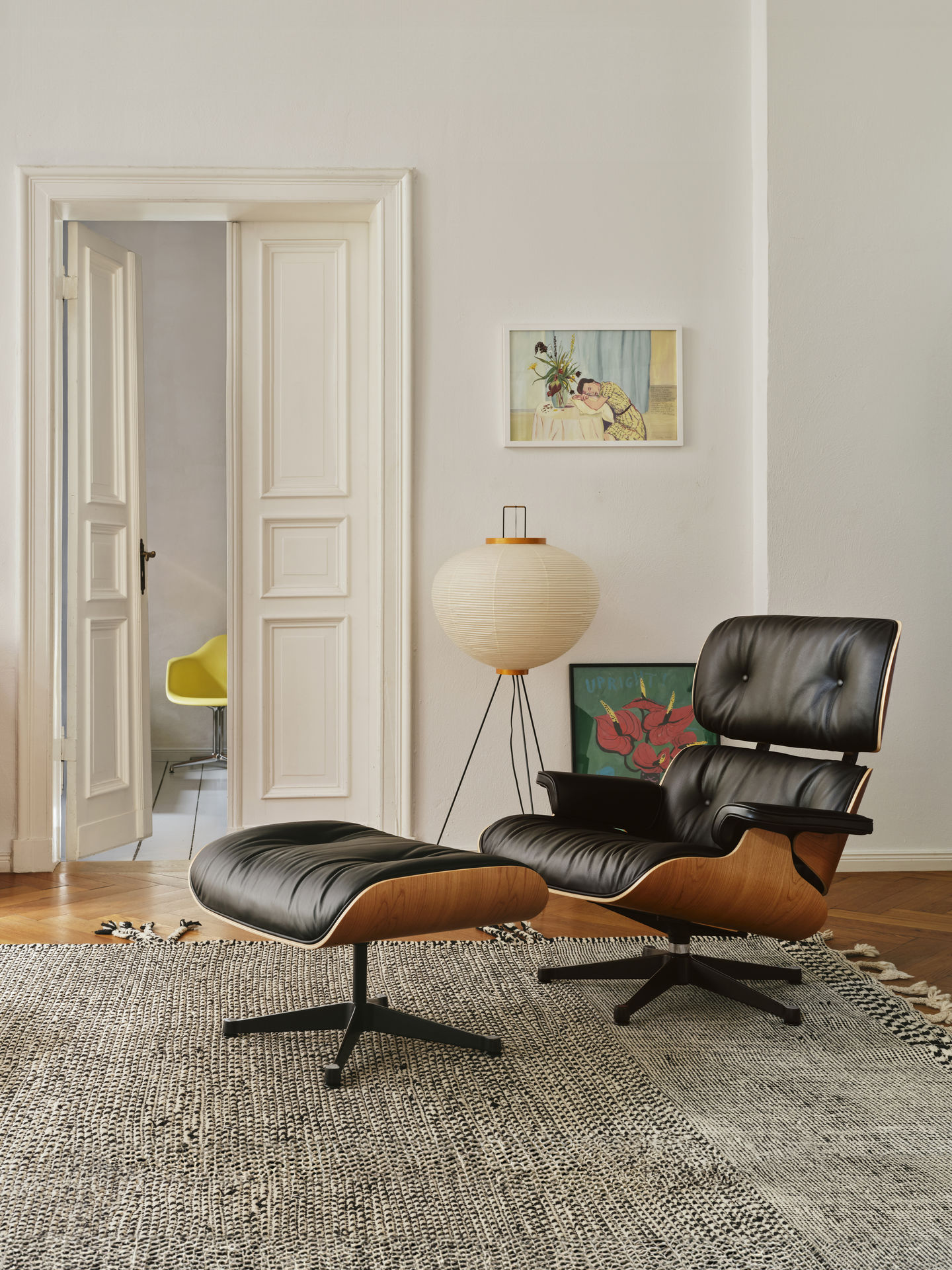 Eames Lounge Chair mit Ottoman in Schwarz und Holz auf Teppich in hellem Raum.