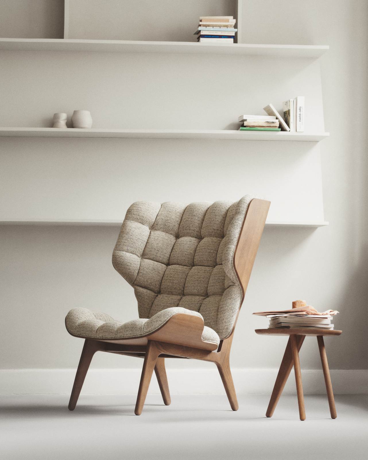 NORR11 Mammoth Chair Sessel mit hellgrauem Stoffbezug und Holzgestell vor weißem Regal.