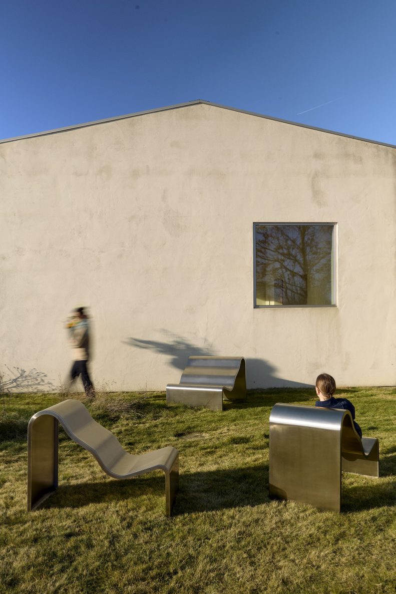 Muuto Dream Bench Outdoor Bank aus Edelstahl auf Rasen vor modernem Gebäude.