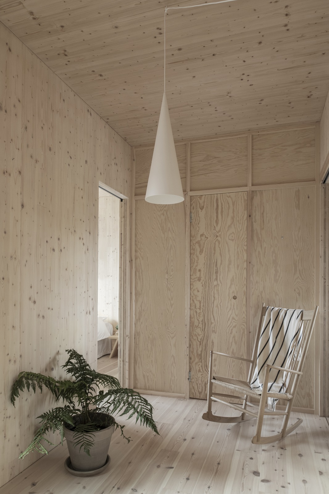 Helle Holzwand mit w221 S1 Medium Pendelleuchte von wästberg, Schaukelstuhl und Zimmerpflanze in modernem Raum.