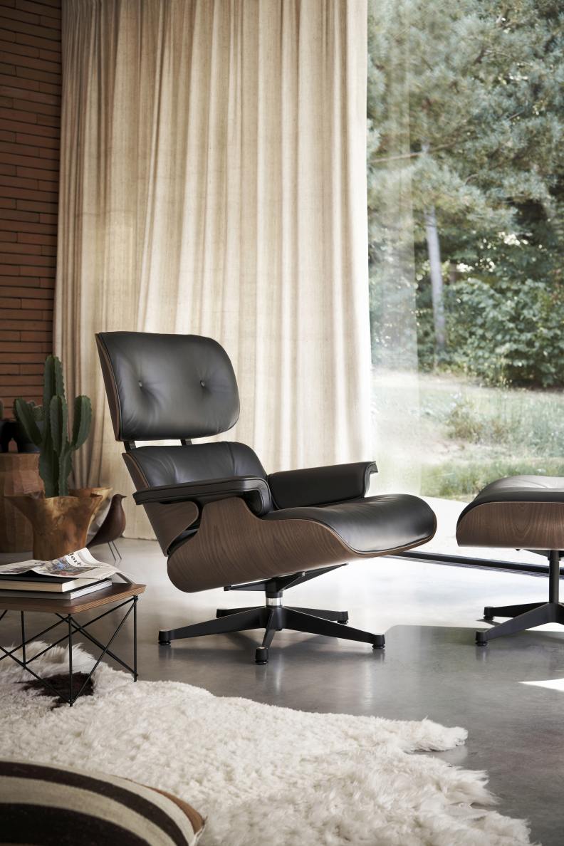 Eames Lounge Chair mit Ottoman in schwarzem Leder und dunklem Holzfurnier vor Fenster.