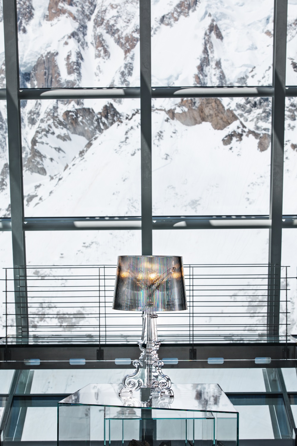 Nahaufnahme der silbernen Kartell Bourgie Tischleuchte mit plissiertem Lampenschirm vor verschneiter Bergkulisse.