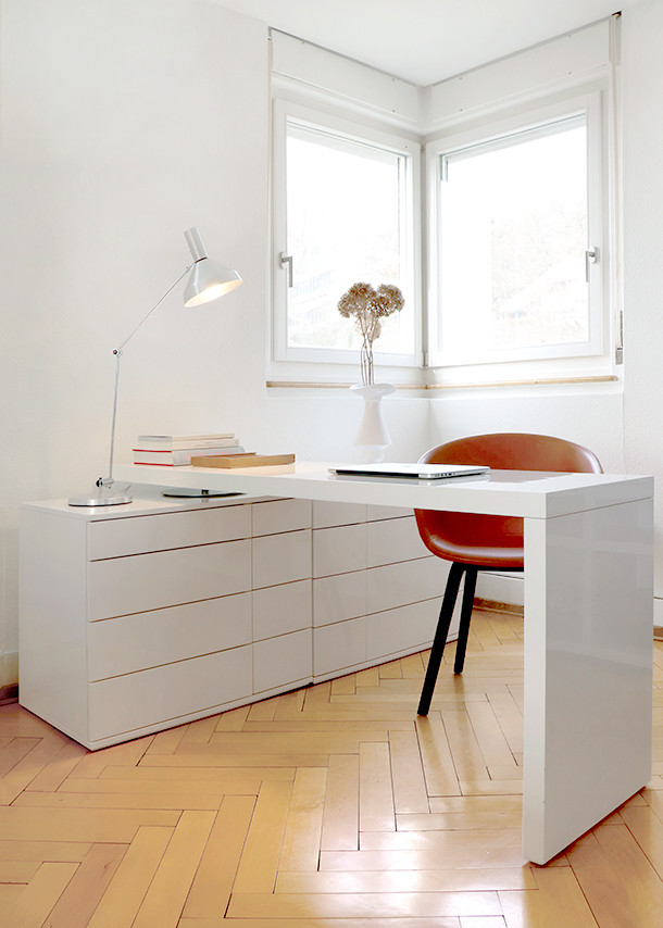 Weißer Schreibtisch mit Schubladen, Lampe und Laptop in modernem Arbeitszimmer mit rotem Stuhl und Parkettboden.