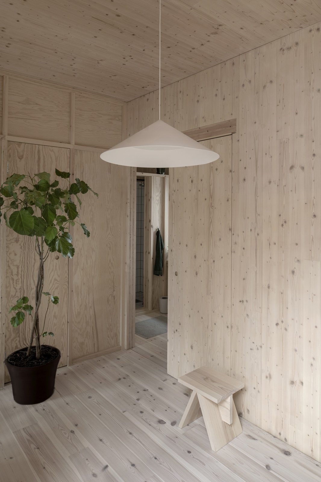 Helle w221 S3 Medium Pendelleuchte von wästberg in einem modern holzvertäfelten Raum mit Pflanze.