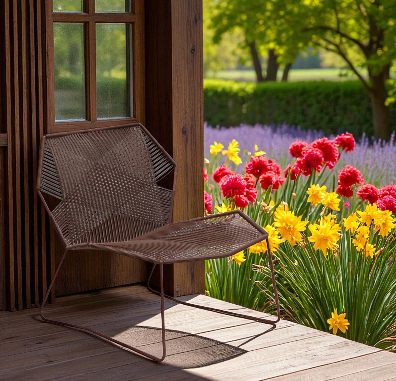 Moroso Tropicalia Sessel für den Außenbereich, brauner Design-Gartenstuhl auf Holzterrasse vor Blumenbeet.
