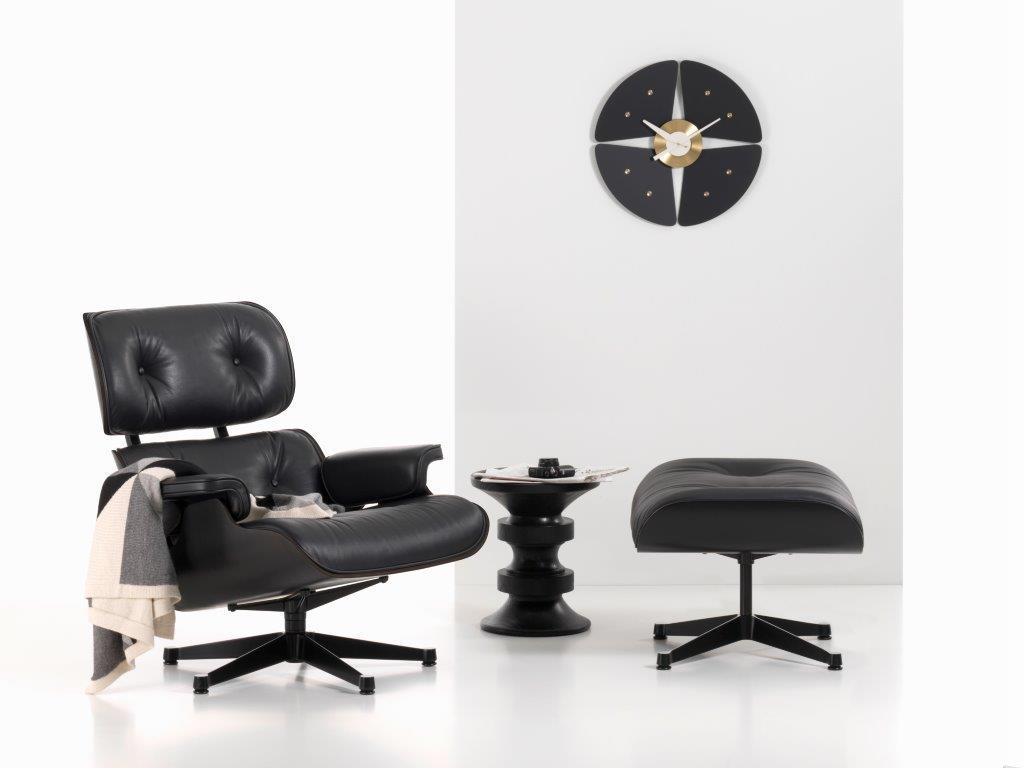 Schwarze Petal Clock Wanduhr von Vitra über einem schwarzen Sessel mit Hocker und Beistelltisch.