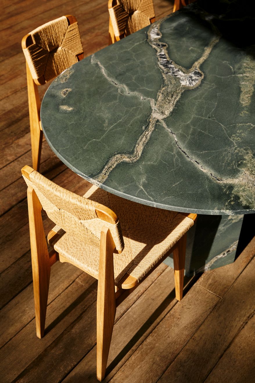 Gubi Epic Outdoor Esstisch aus grünem Marmor mit passenden Stühlen auf einer Holzterrasse.