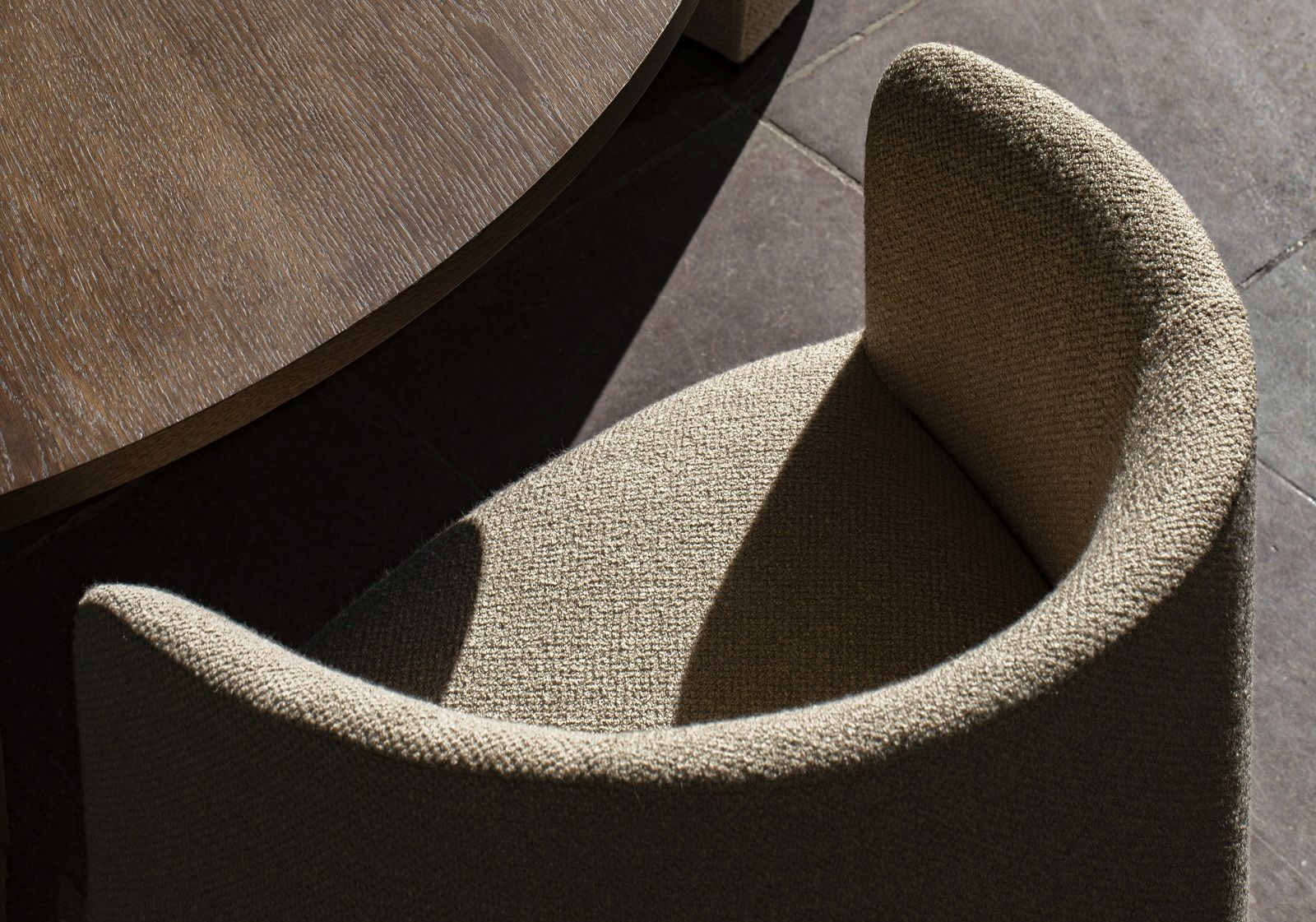 Detailaufnahme von Tearoom Lounge Chair Sessel Audo Copenhagen mit beigem Stoffbezug und Holztischplatte im Hintergrund.