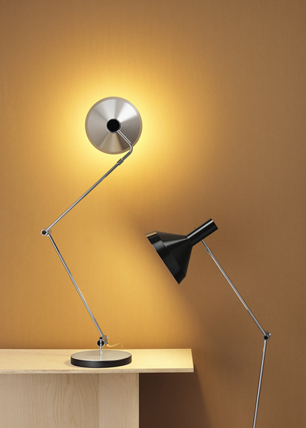 Silberne Schreibtischlampe mit Gelenkarm und schwarze Stehlampe vor ockerfarbenem Hintergrund.