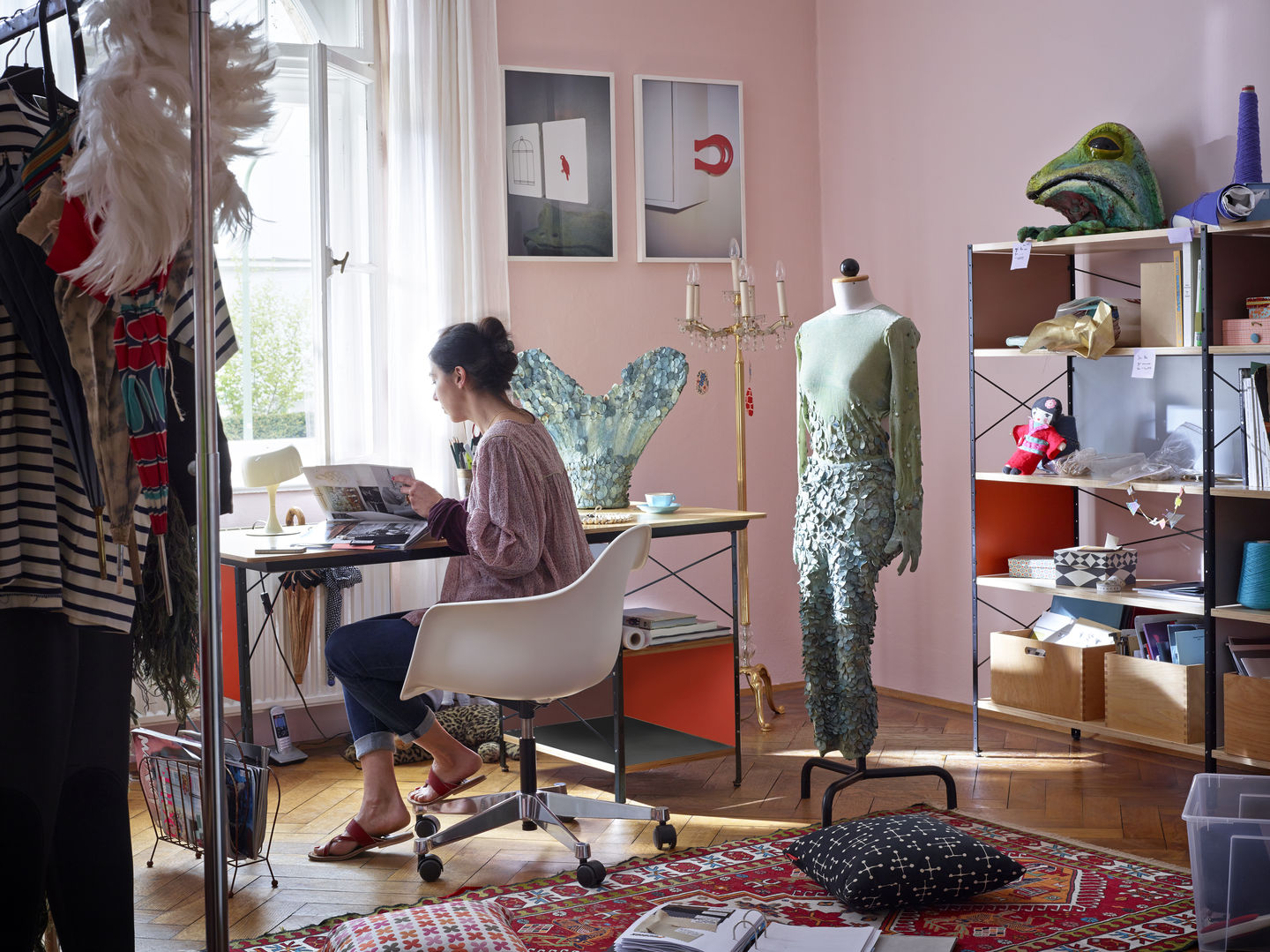 Frau sitzt auf einem weißen Eames Stuhl am Schreibtisch in einem Atelier.