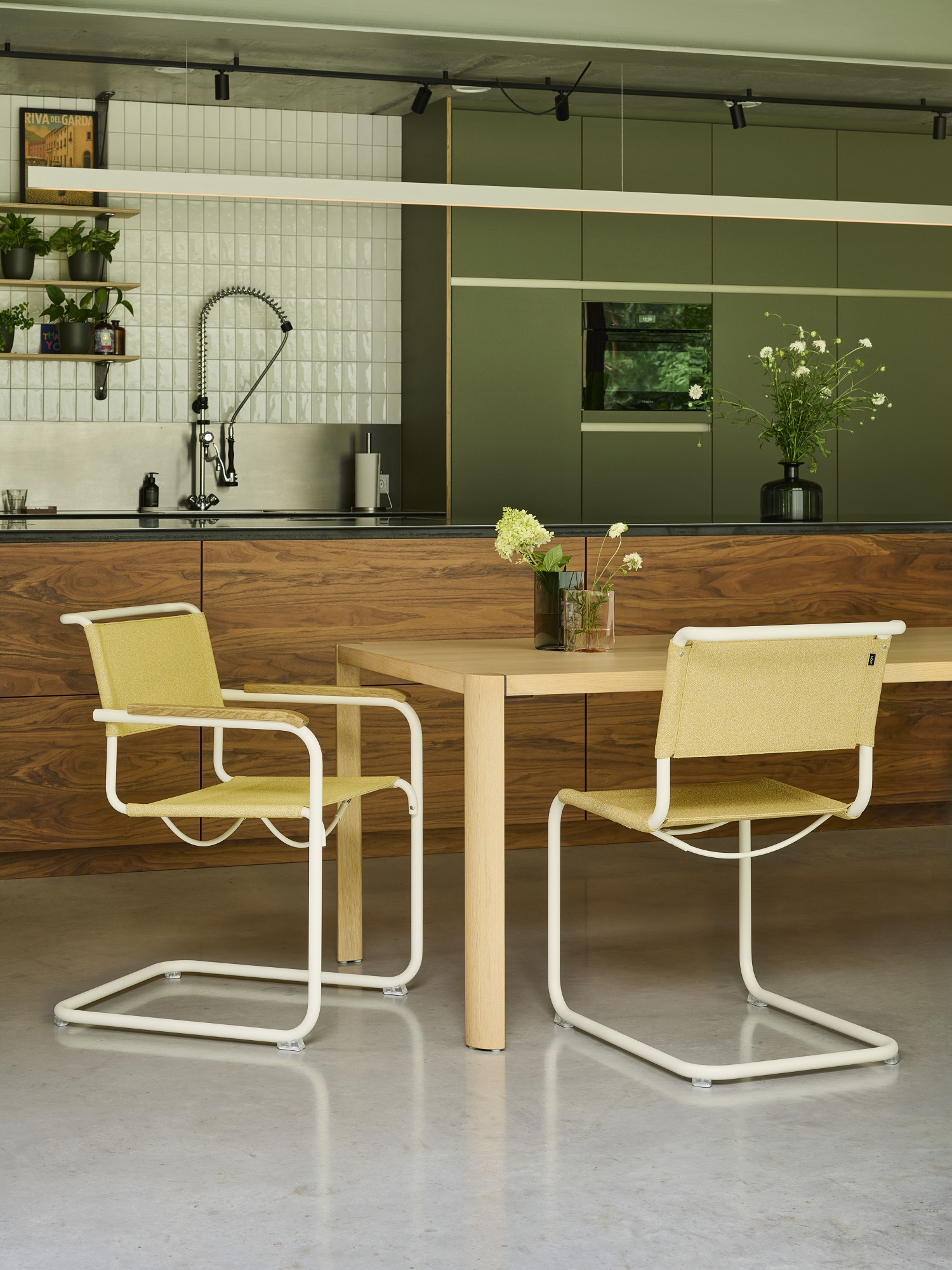 Zwei Thonet S 34 Freischwinger Stühle mit gelbem Stoffbezug und weißem Stahlrohrgestell an Esstisch.