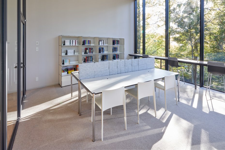 Heller Büroraum mit USM Haller Regalsystem, Schreibtisch mit Privacy Panels und weißen Stühlen.