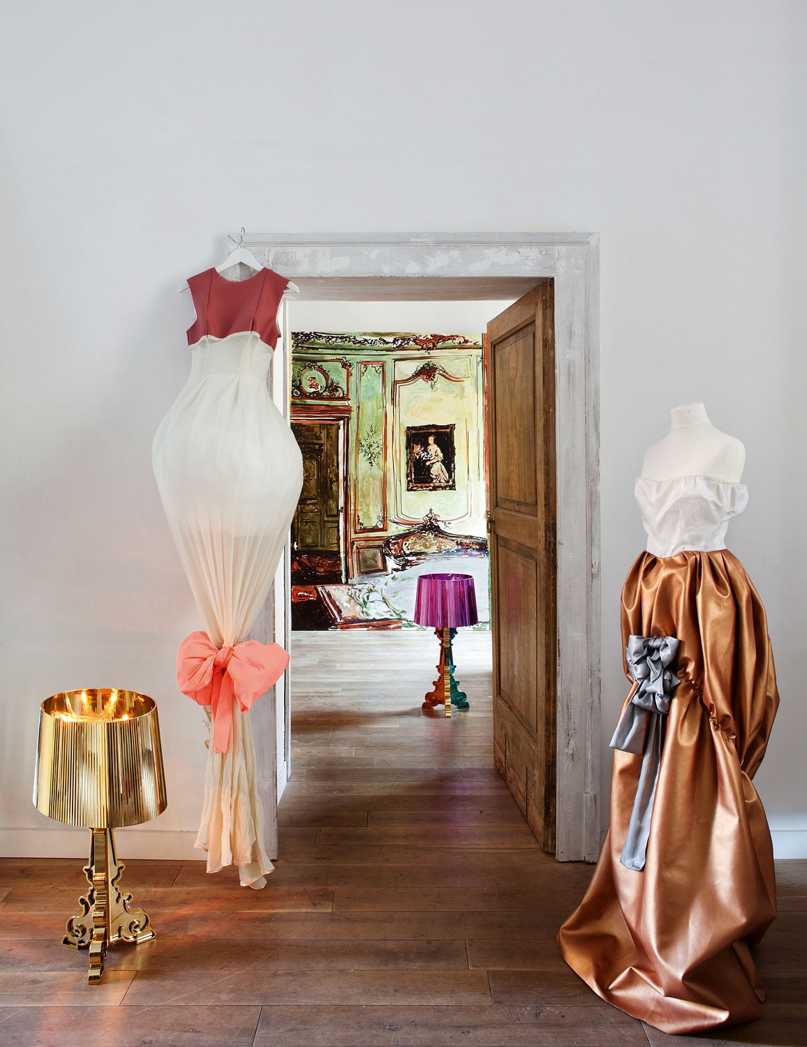 Dekoratives Interieur mit Kartell Bourgie Tischleuchte in metallischem Kupfer neben Kleiderpuppen und Blick in ein kunstvolles Zimmer.