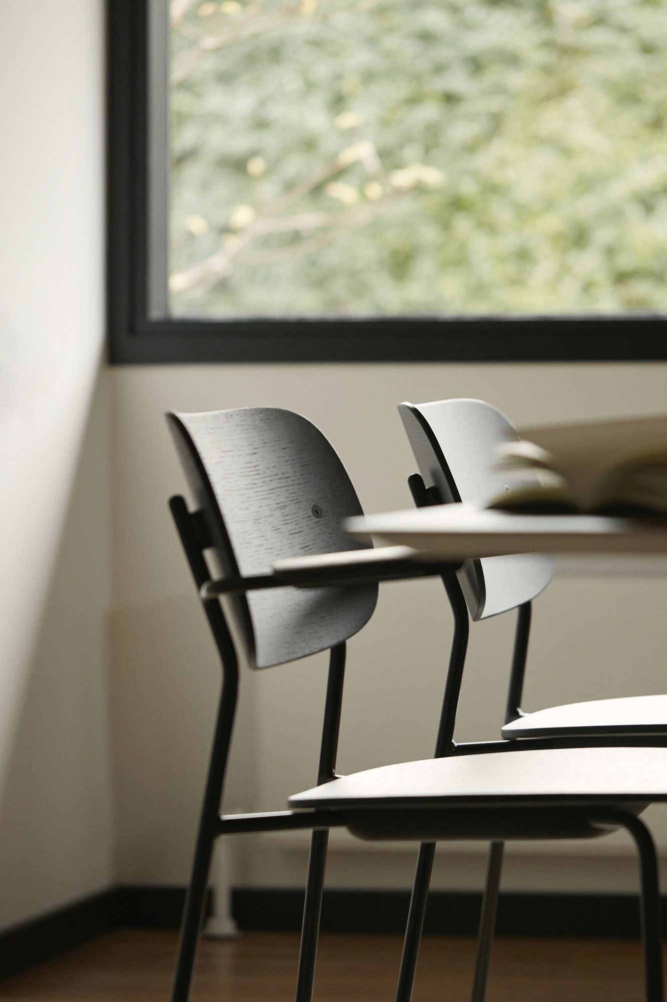Nahaufnahme von zwei Co Dining Chairs von Audo Copenhagen mit schwarzem Metallgestell und Holzlehne.