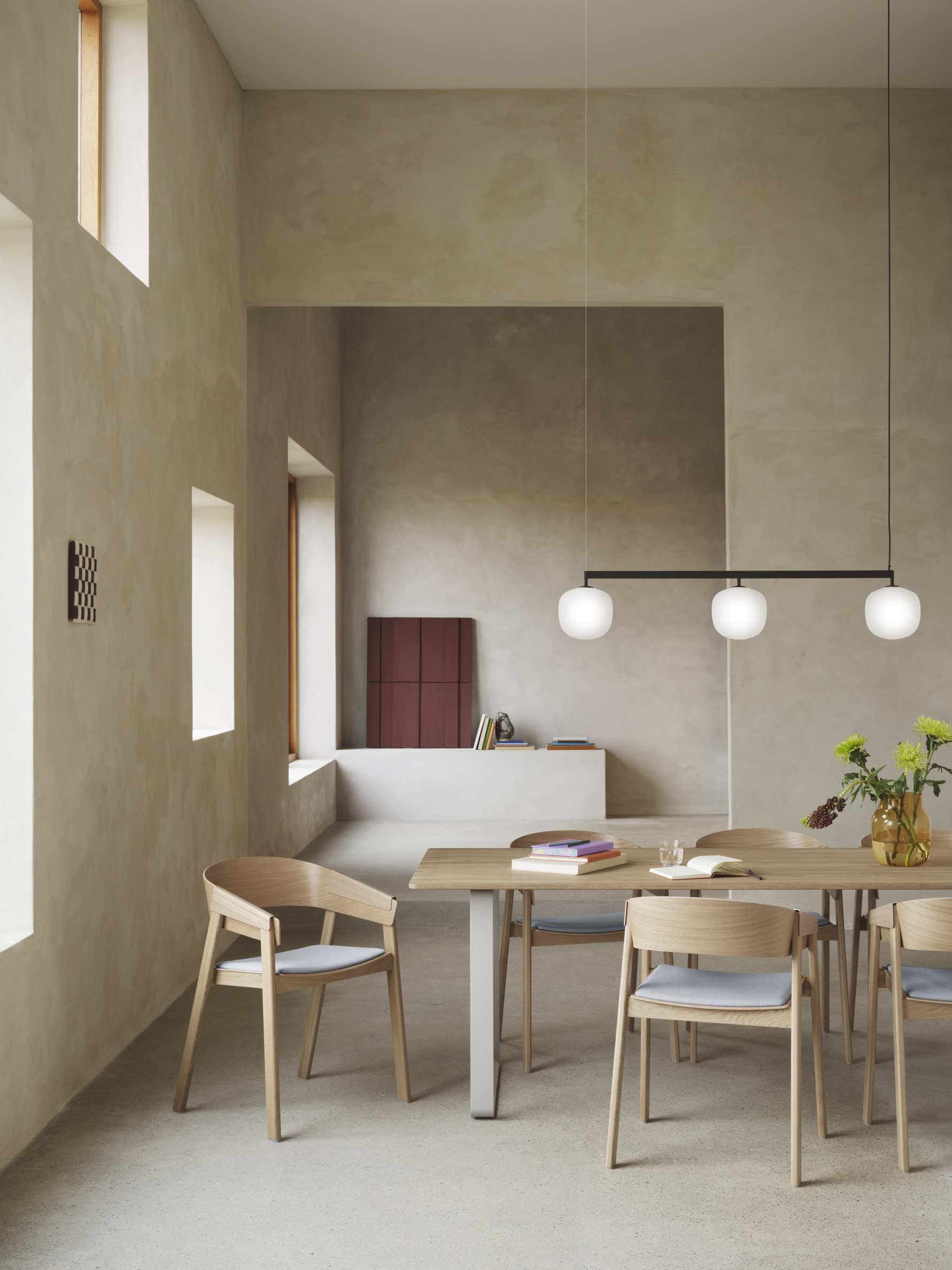 Helle Esszimmer-Szene mit Muuto Rime Rail Pendelleuchte, die über einem Holztisch mit Stühlen hängt.