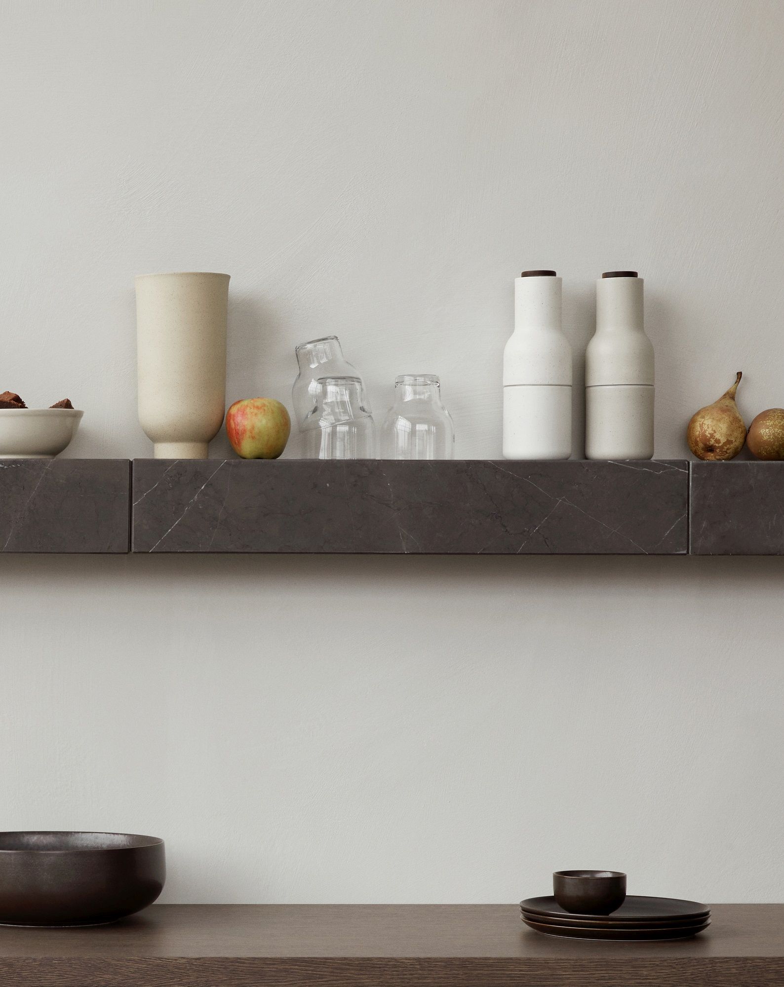 Audo Copenhagen Plinth Shelf Regal aus dunklem Marmor mit Deko-Elementen wie Geschirr und Obst.