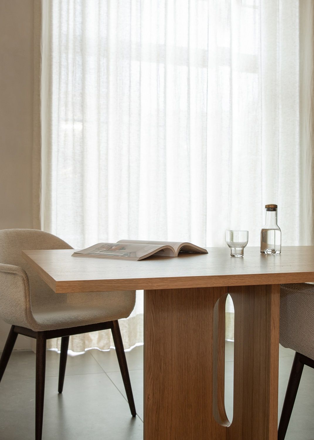 Nahaufnahme eines Harbour Dining Chair Stuhls von Audo Copenhagen am Esstisch mit Wasserflasche und Magazin.