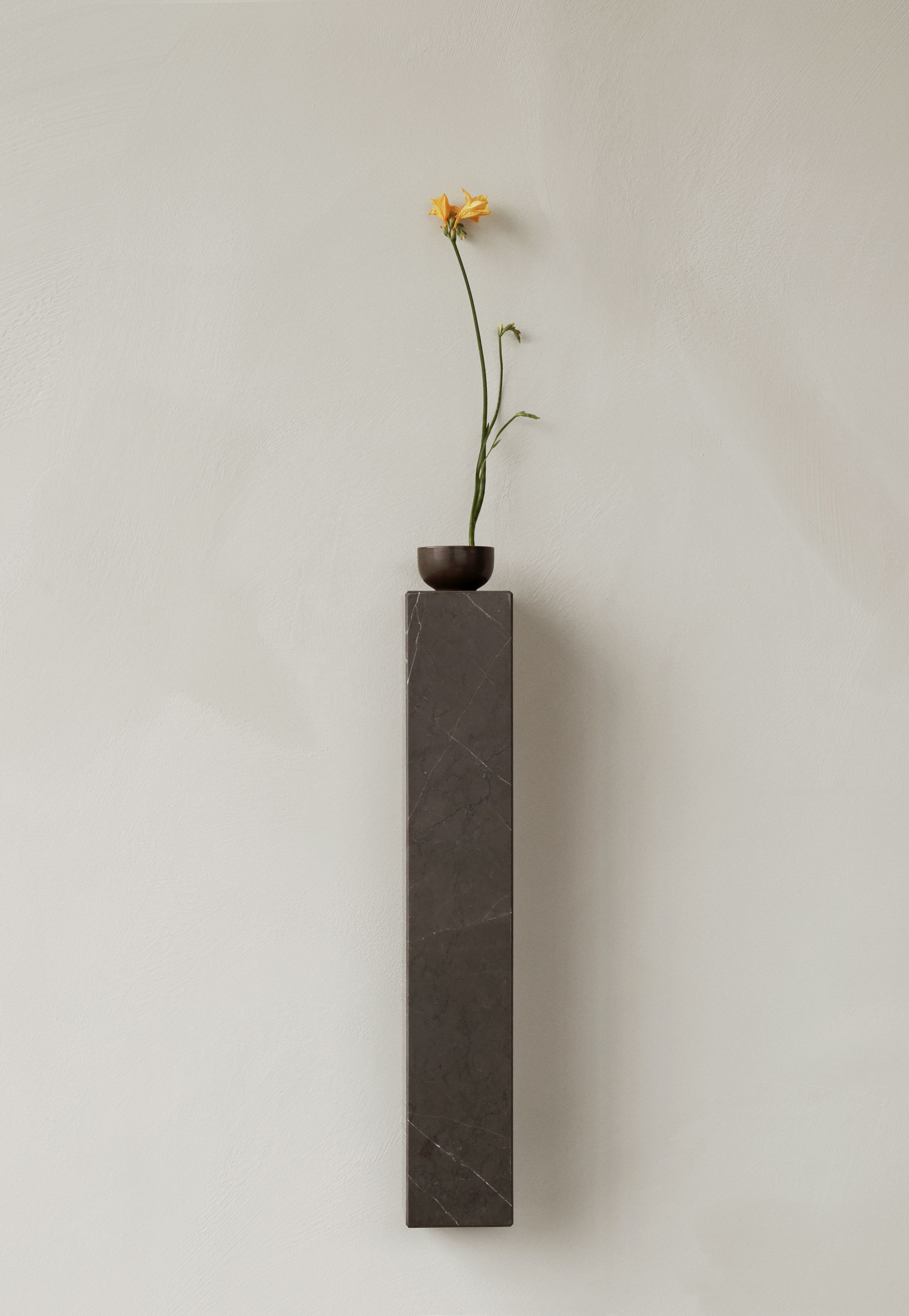 Audo Copenhagen Plinth Shelf Regal aus Marmor mit gelber Blume in dunkler Vase.