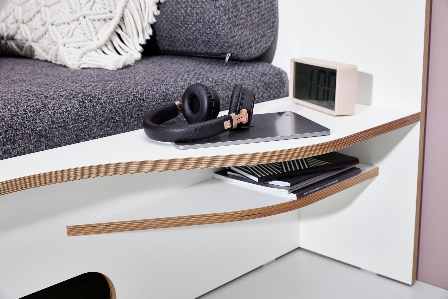 Detailaufnahme vom Müller Möbelwerkstätten Plane Einzelbett mit Ablage, Kopfhörern, Tablet und Notizbüchern.