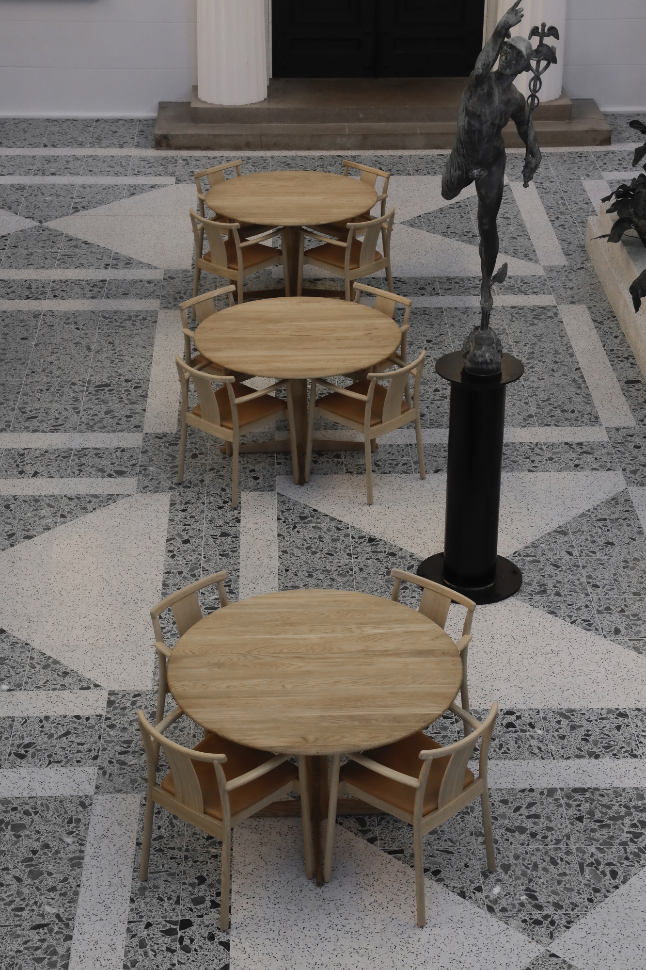 Draufsicht auf drei Tische mit Audo Copenhagen Merkur Dining Chairs Stühlen mit Armlehnen im Außenbereich.