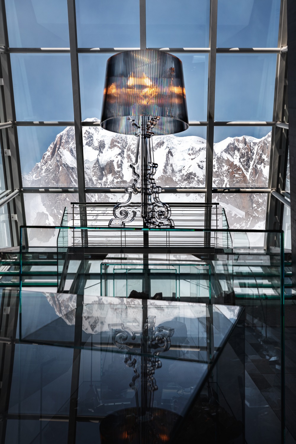 Nahaufnahme der silbernen Kartell Bourgie Tischleuchte mit geripptem Lampenschirm vor Bergpanorama.