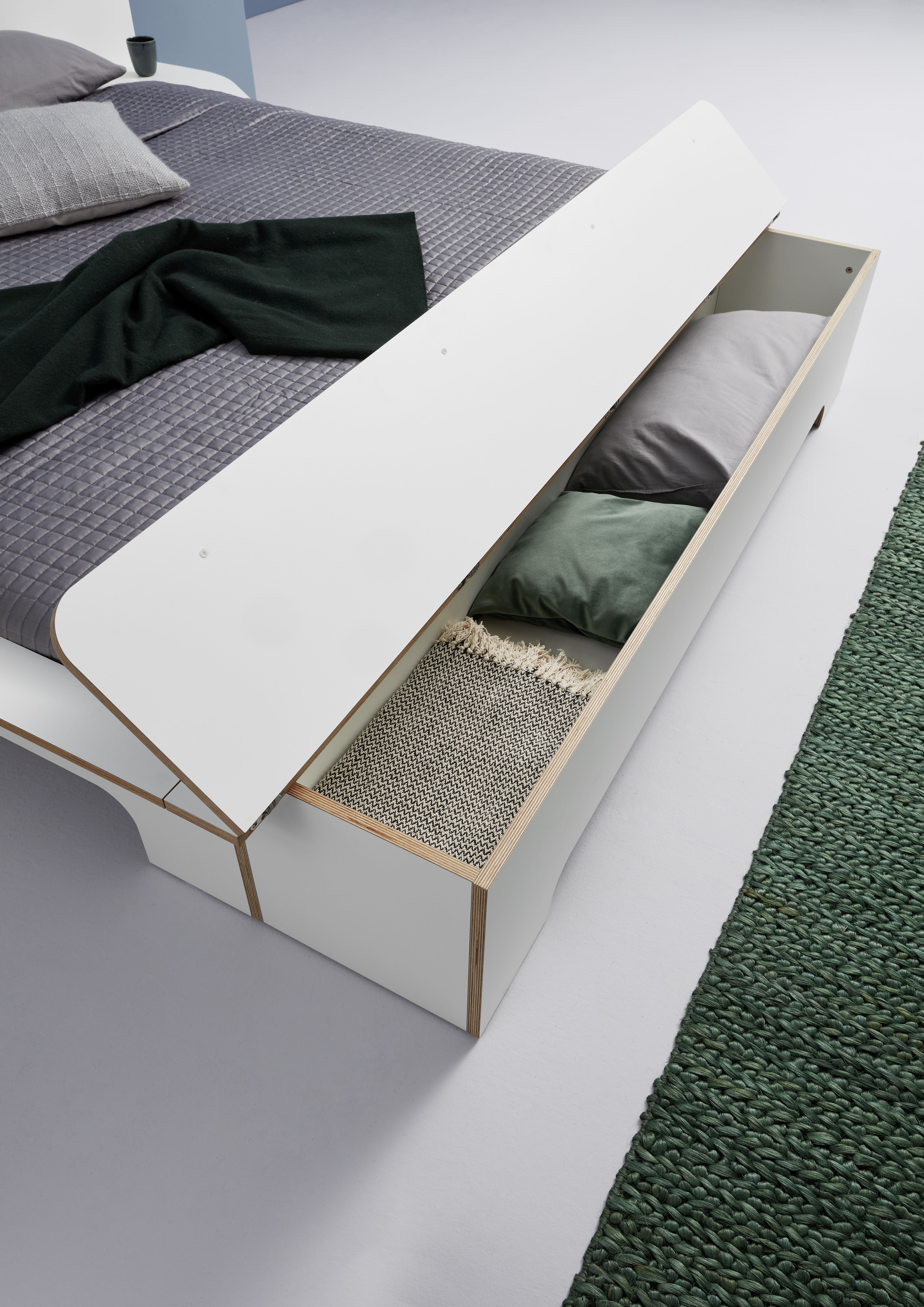 Plane Doppelbett von Müller Möbelwerkstätten mit geöffnetem Bettkasten, der Kissen und eine Decke zeigt.