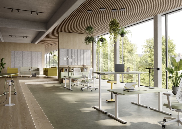 Helles Büro mit Palmberg Sitz-Stehtischen in Grün und Weiß, Laptops und Büropflanzen vor Fensterfront.