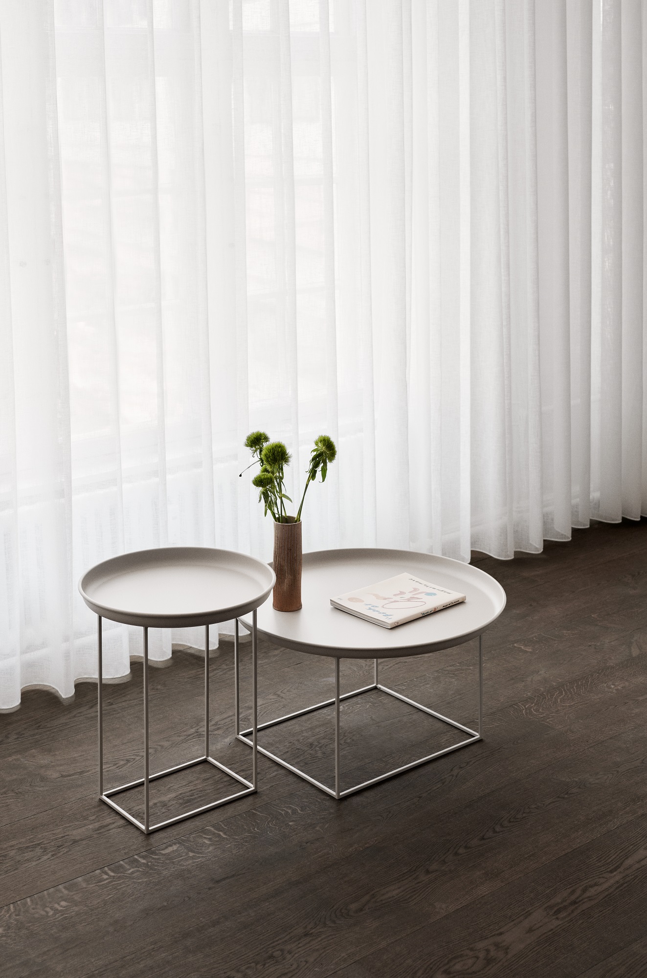 Norr11 Duke Beistelltisch Set: Kleiner, grauer runder Tisch mit Blumen und Buch vor Fenster.