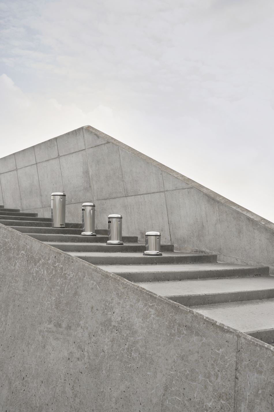 Vier Vipp Treteimer aus Edelstahl, 30L, auf einer Betontreppe vor einer Betonwand.