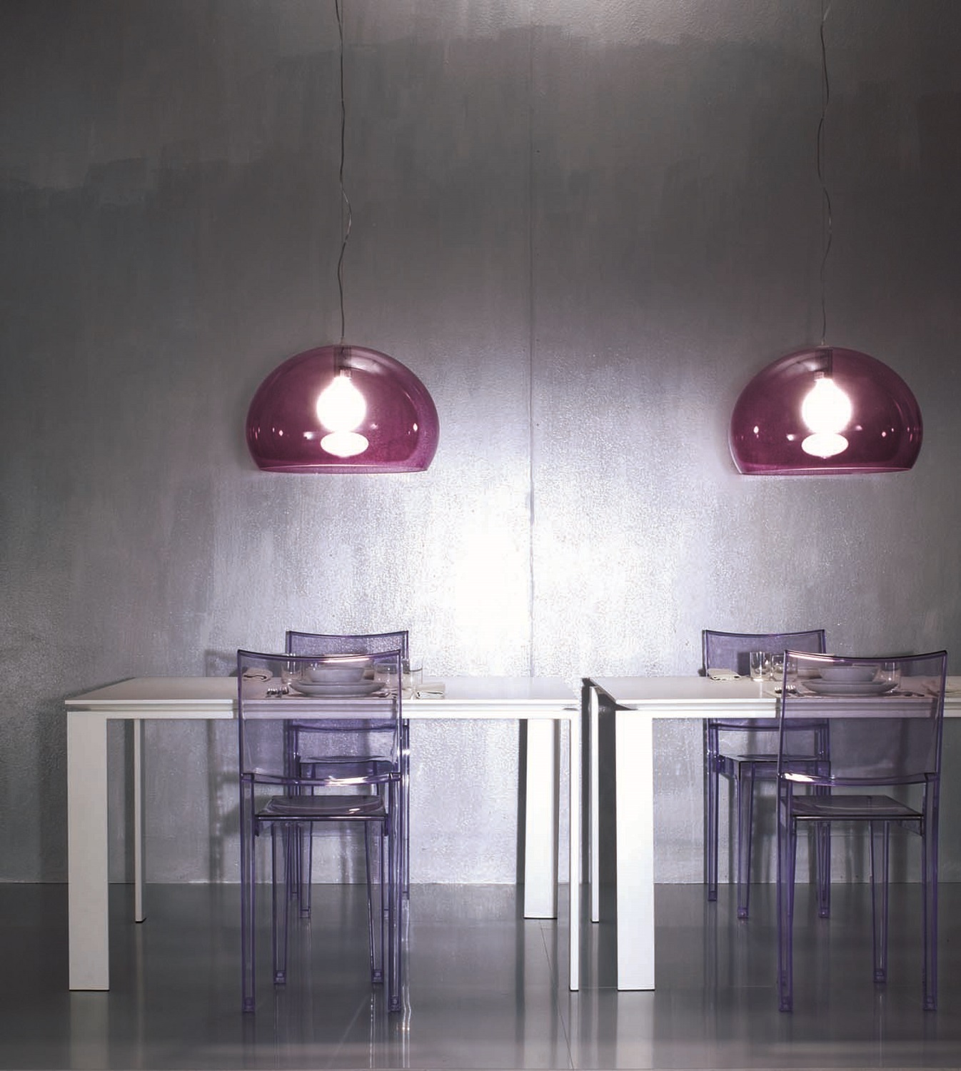 Zwei violette Kartell FL/Y Pendelleuchten über einem Esstisch mit transparenten Stühlen, modernes Wohnraumdesign.