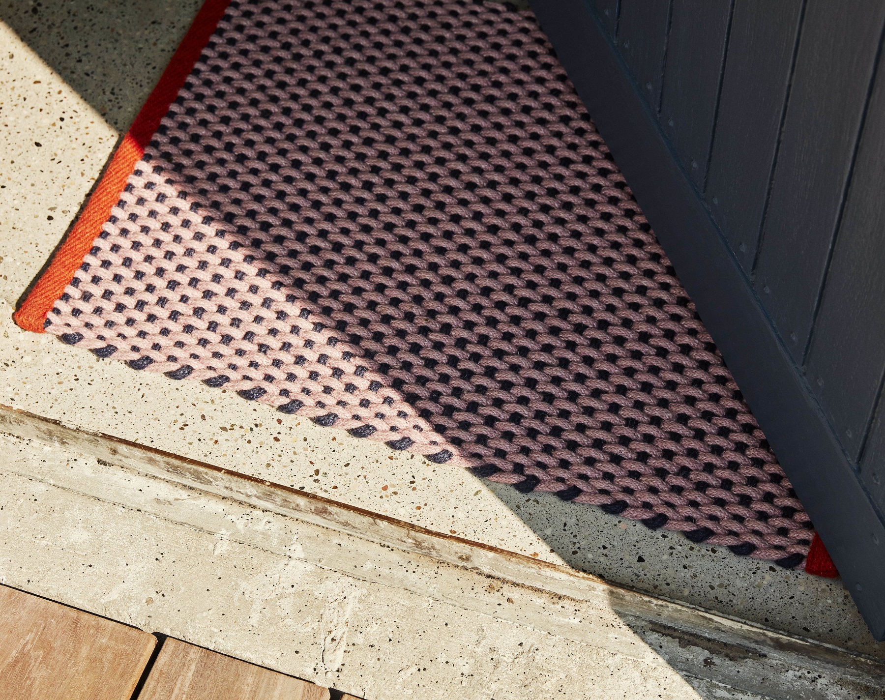 Nahaufnahme des Hay Door Mat Teppichs in Rosa und Schwarz mit rotem Rand vor einer Haustür.