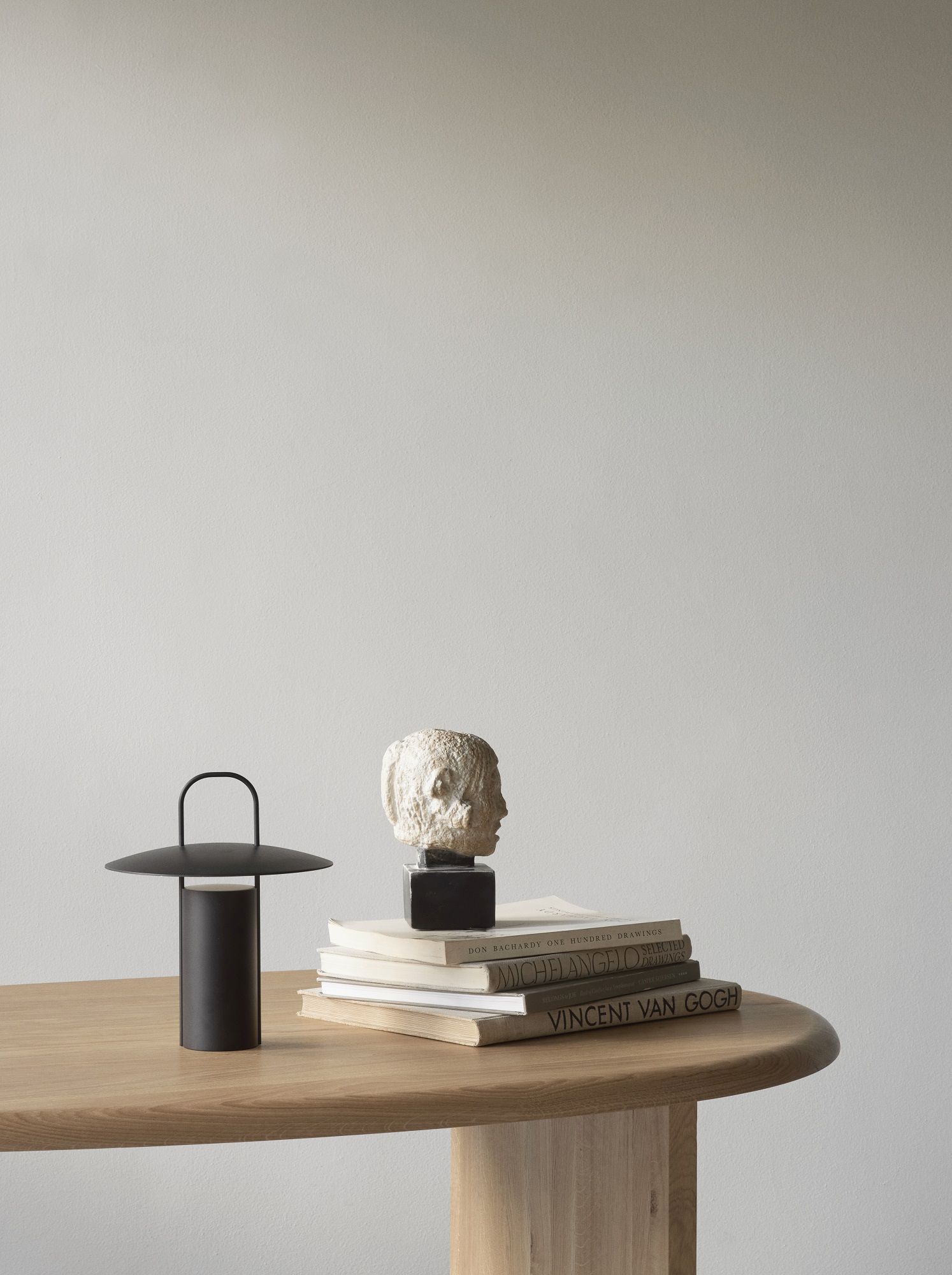 The Eclipse Desk Schreibtisch von Audo Copenhagen auf einem Holztisch mit Büchern und Skulptur.