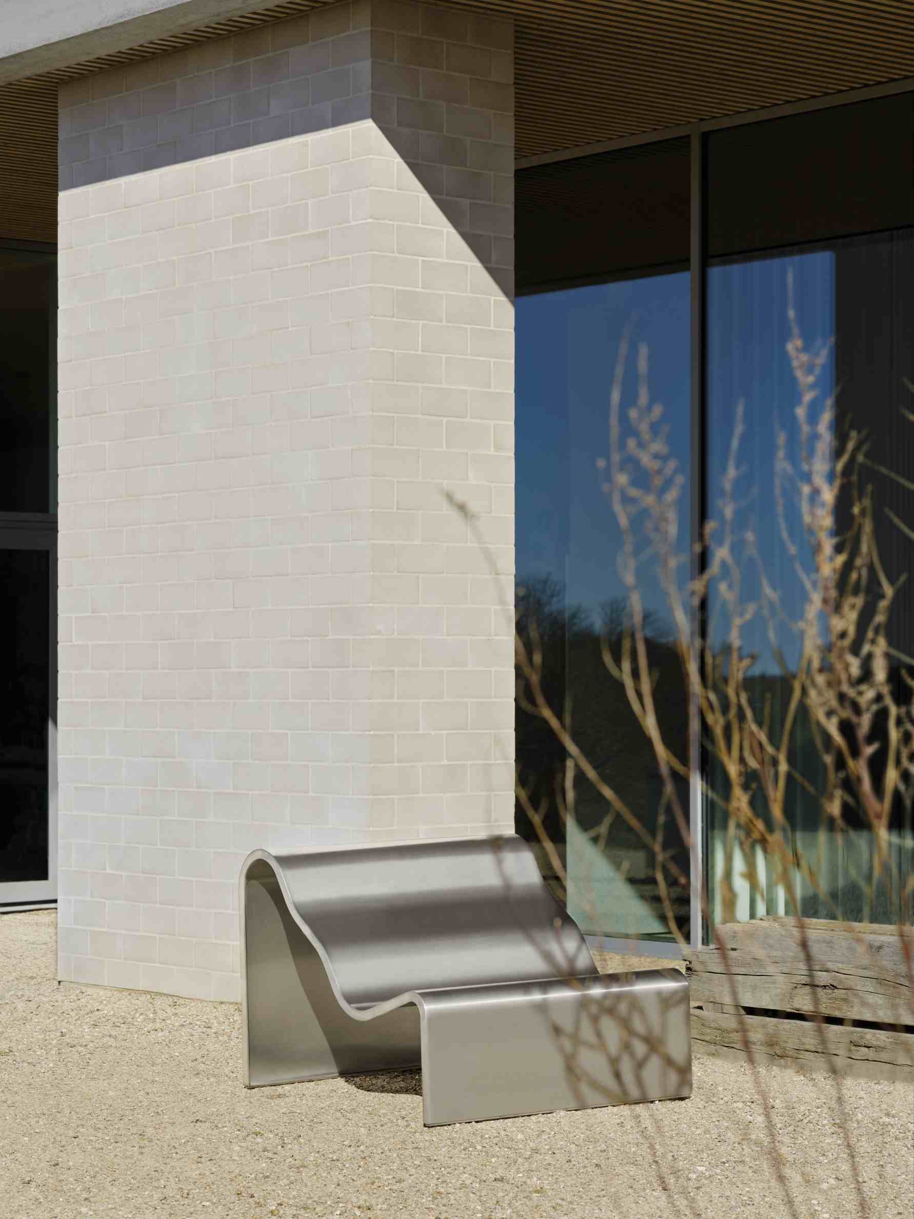 Muuto Dream Bench Outdoor Bank aus Edelstahl vor modernem Gebäude mit Fensterfront.