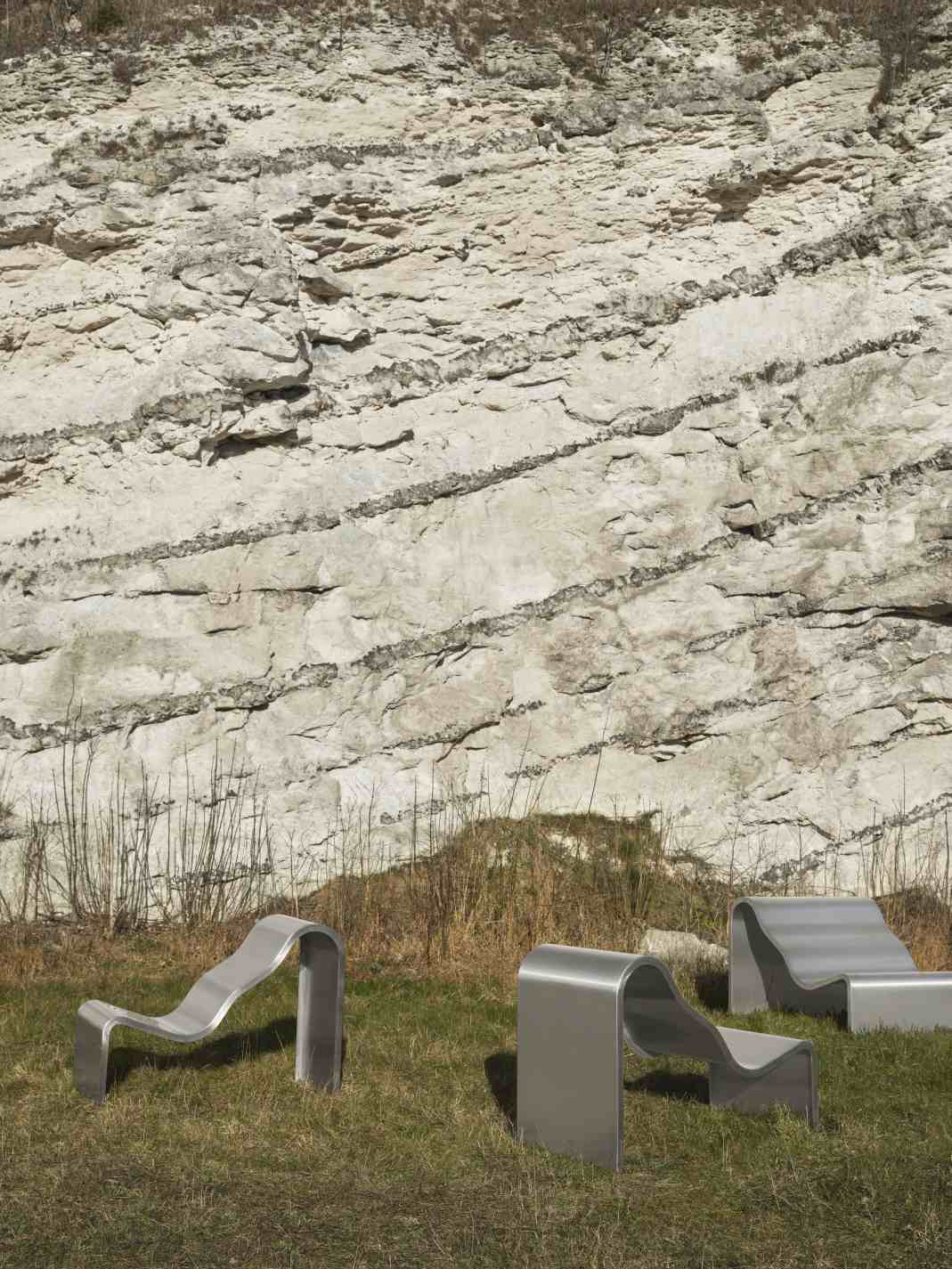Muuto Dream Bench Outdoor Bank aus gebogenem Metall vor einer Felswand auf einer Wiese.