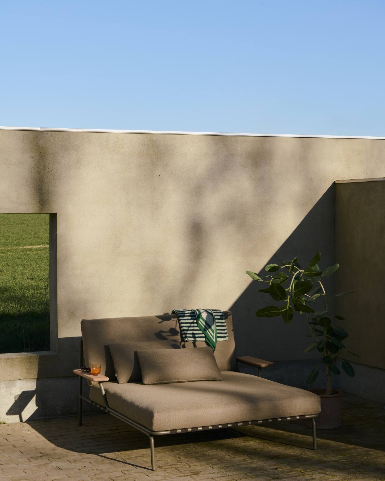 Muuto Settle Lounge Bed Outdoor Liege mit Kissen und Getränk im Garten, modernes Design.