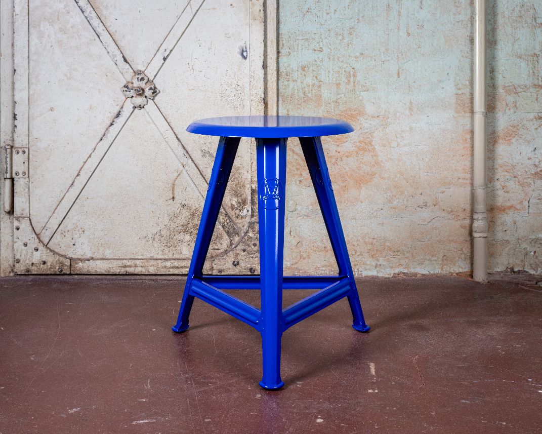 Blauer Rowac Schemel IS 48 cm Hocker Blueprint Edition vor einer weißen Tür und Wand.
