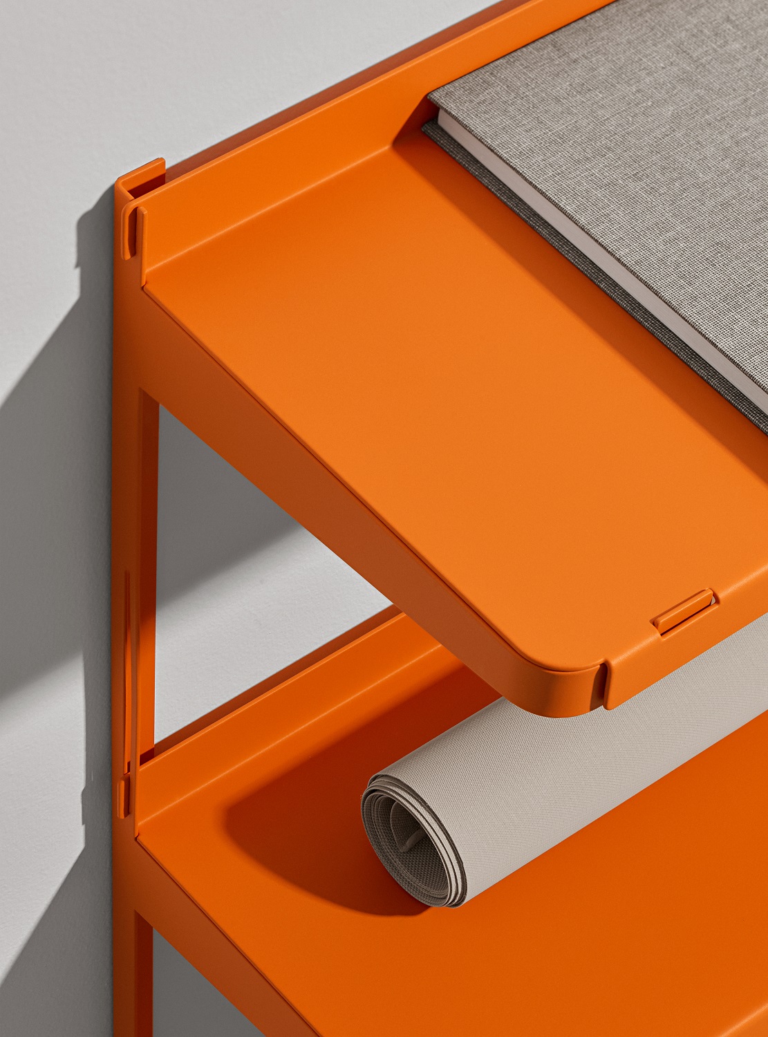 Detailaufnahme des orangefarbenen New Tendency Click Wandregals mit Buch und gerollter Matte.