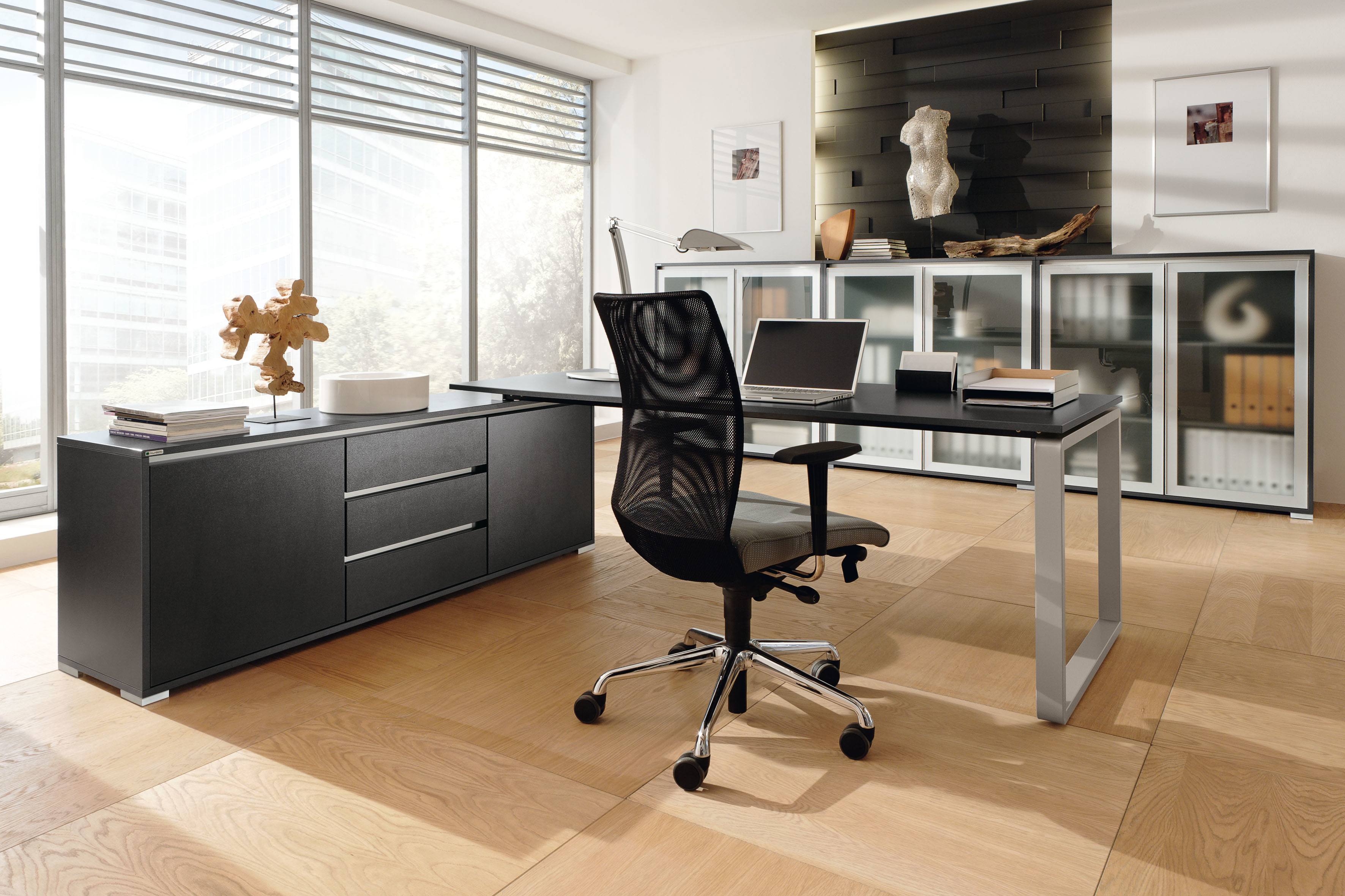 Büro mit Palmberg Schreibtisch, schwarzem Bürostuhl und Sideboard vor Fenster. Modernes Bürodesign.