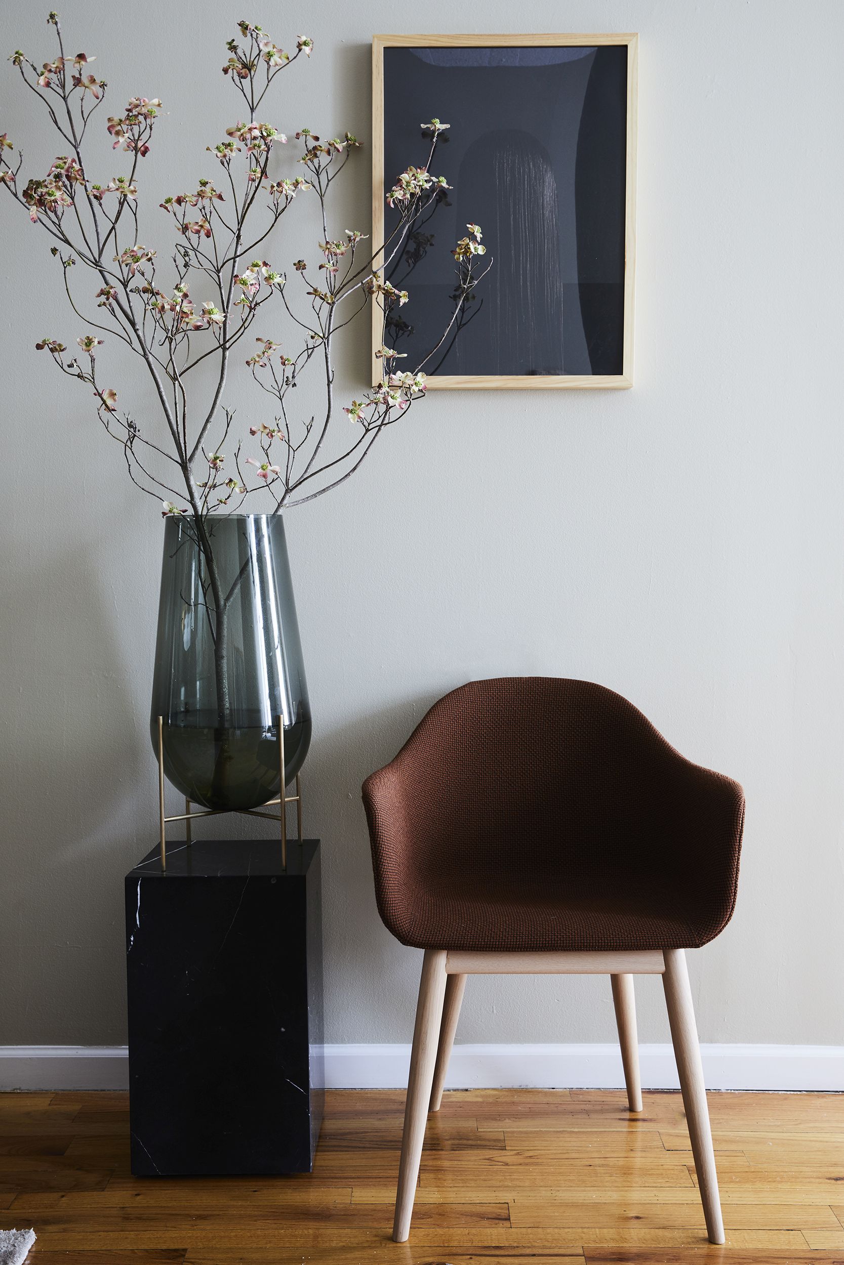 Brauner Audo Copenhagen Harbour Dining Chair Stuhl mit Holzbeinen neben Blumenvase und Kunstwerk.